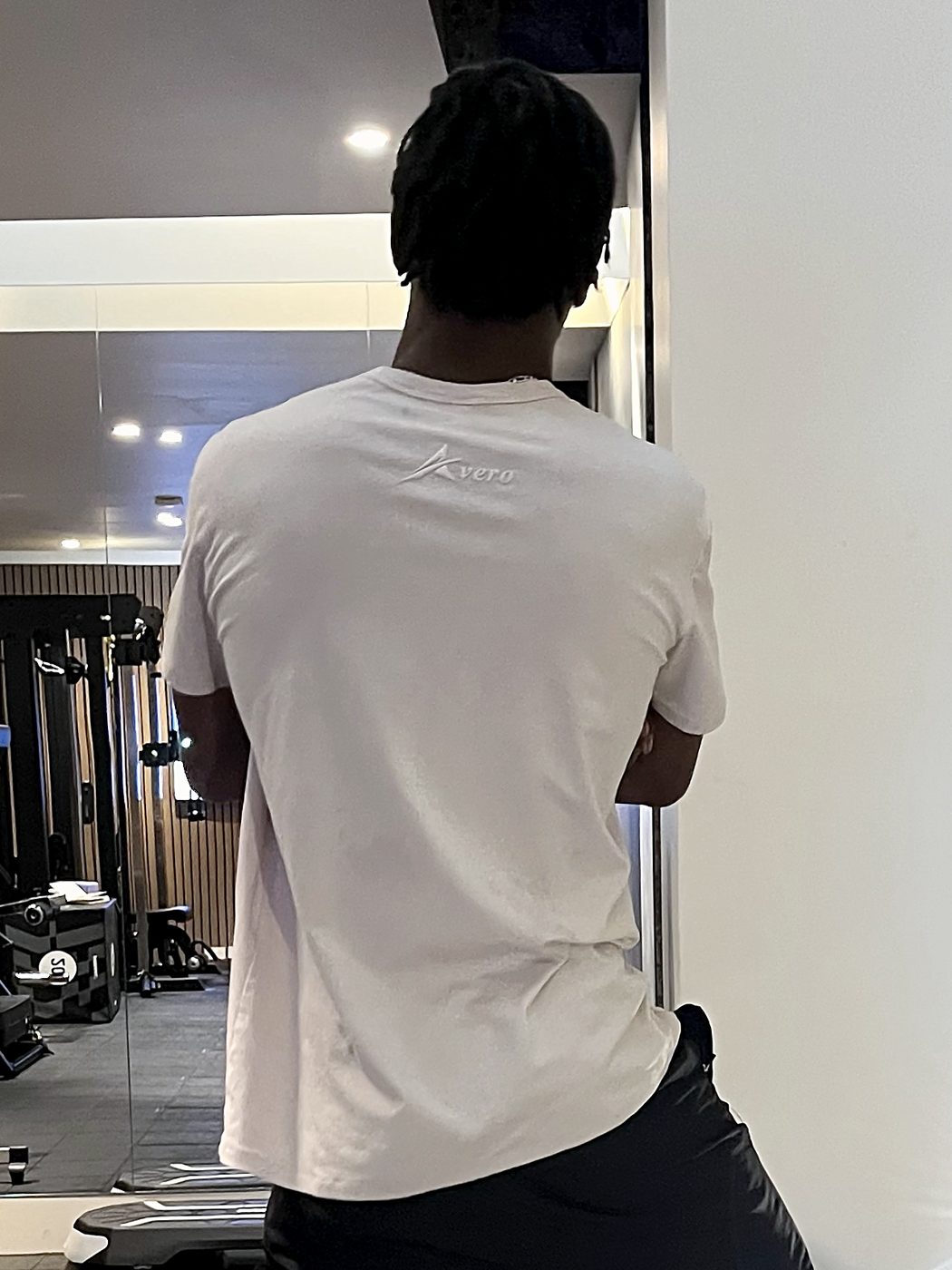 Back view of the Origin Tee in Sand, worn in the gym, with the tonal Avero logo below the collar