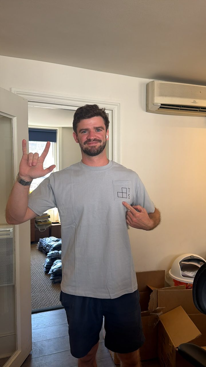 A Thornhill Shann team member pointing to the TS mark on the pocket of a grey tee